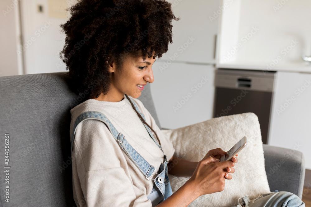 Smiling woman sitting on couch at home using cell phone Smiling woman sitting on couch at home using cell phone