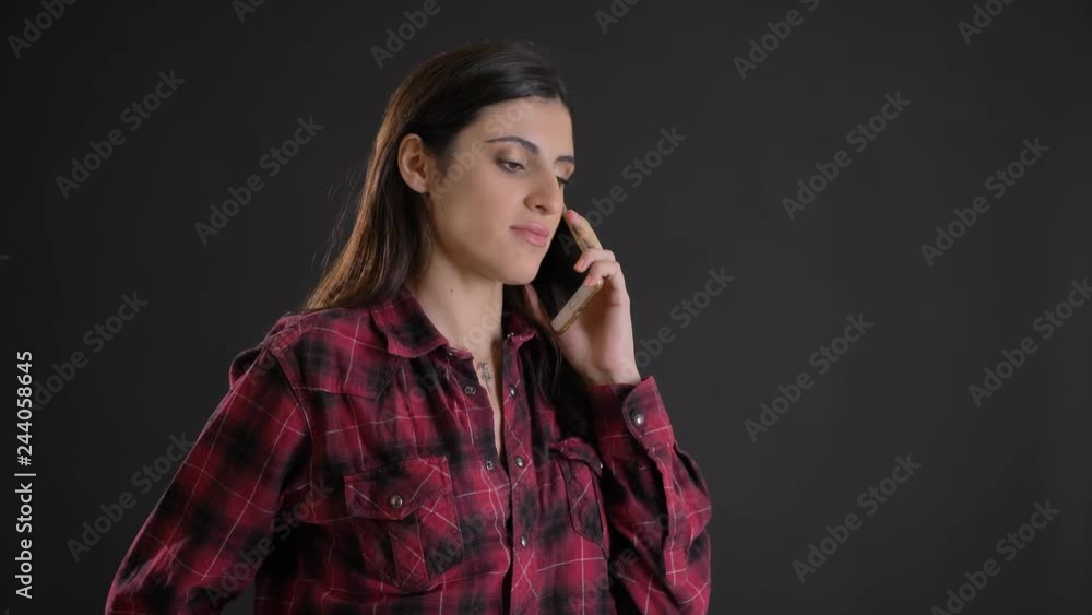 Portrait of young and beautiful caucasian long-haired girl attentively talking on cellphone on black background.