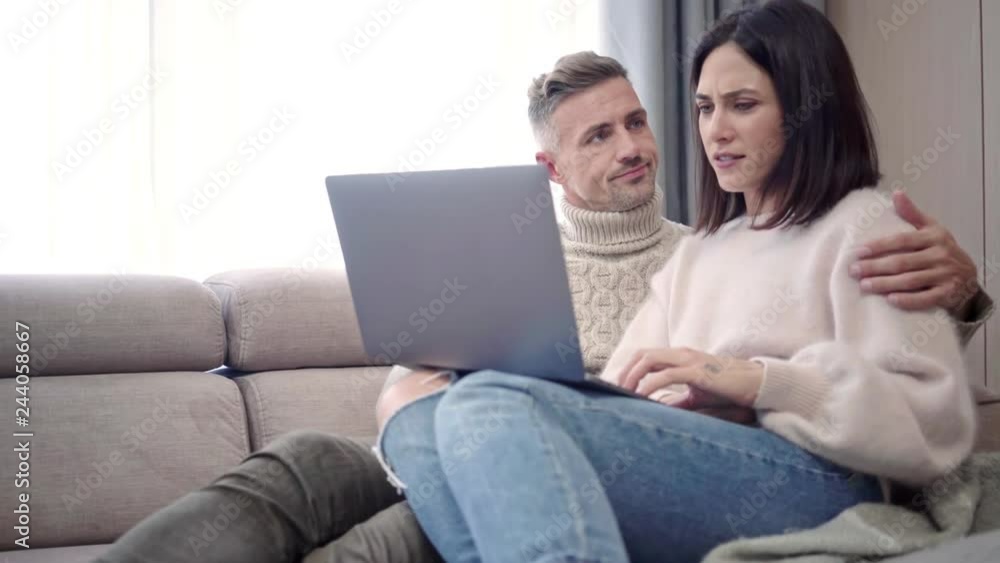Happy lovely couple using laptop computer while sitting on sofa at home Happy lovely couple using laptop computer while sitting on sofa at home