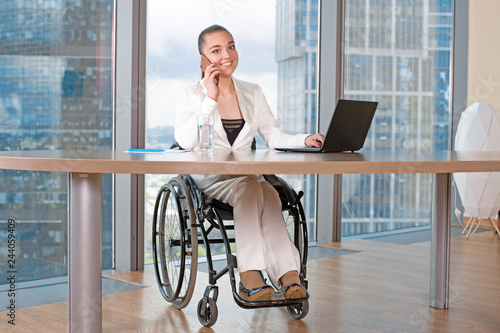 Invalid or disabled young business woman person sitting wheelchair working in office on a laptop