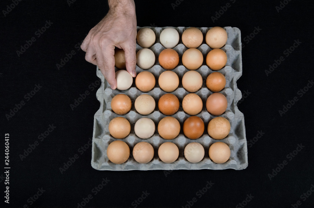Male hand taking one egg from cardboard egg box on black mat background Male hand taking one egg from cardboard egg box on black mat background