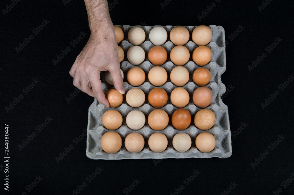 Male hand taking one egg from cardboard egg box on black mat background Male hand taking one egg from cardboard egg box on black mat background