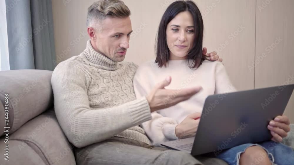 Happy lovely couple talking by videocall on laptop computer while sitting together on sofa at home Happy lovely couple talking by videocall on laptop computer while sitting together on sofa at home