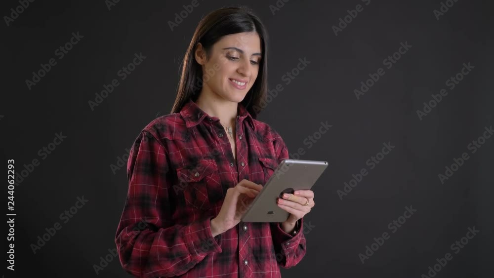 Portrait of young and beautiful caucasian long-haired girl smilingly watching into tablet on black background. Portrait of young and beautiful caucasian long-haired girl smilingly watching into tablet on black background.