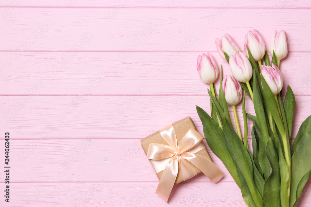 Fototapeta premium A bouquet of beautiful tulips and a gift on a wooden background top view. Mother's Day Background, International Women's Day. Holiday, give a gift.