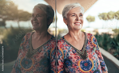 Portrait of a beautiful grey haired middle aged woman looking out into the distance with her reflection