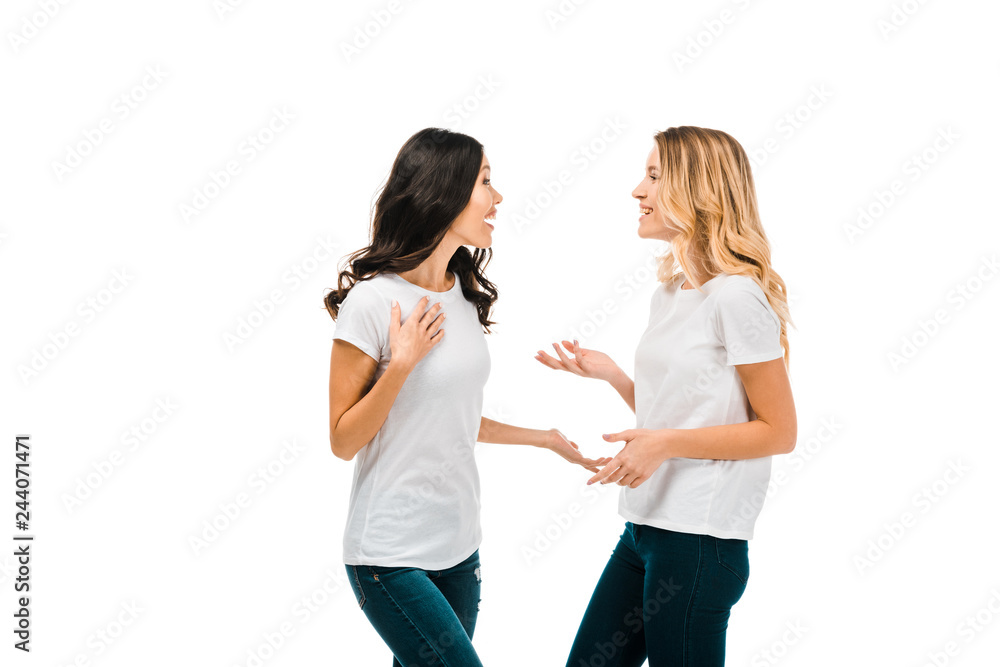 happy young women in white t-shirts talking and looking at each other isolated on white