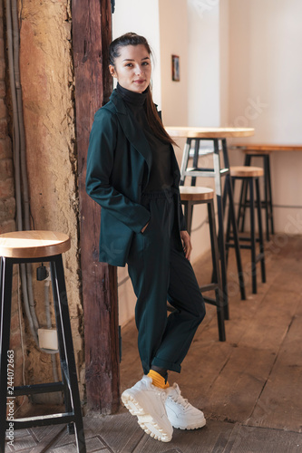 Portrait of elegant pensive young brunette woman. dressed in a stylish dark green suit with a jacket, pants and golf. Business young girl, student, teenager, business lady