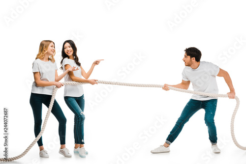 smiling young women and concentrated man pulling rope isolated on white
