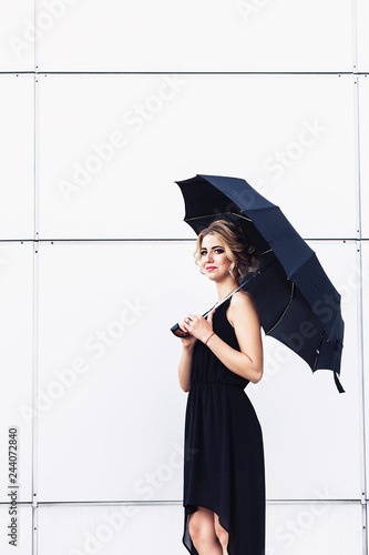 elegant young girl in a black dress and with an umbrella posing against a gray wall.