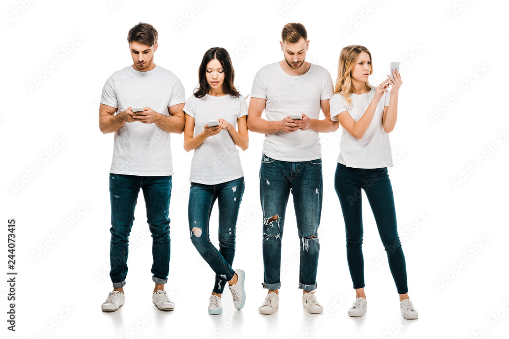Obraz premium full length view of young friends in white t-shirts and jeans using smartphones isolated on white