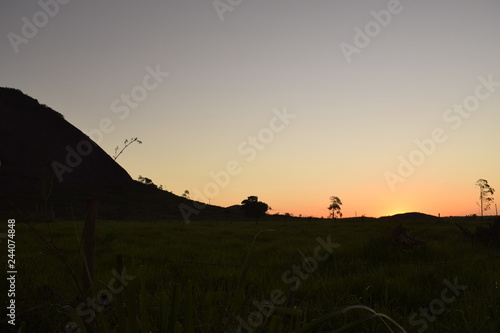 P  r-do-sol laranja em horizonte rural com colina