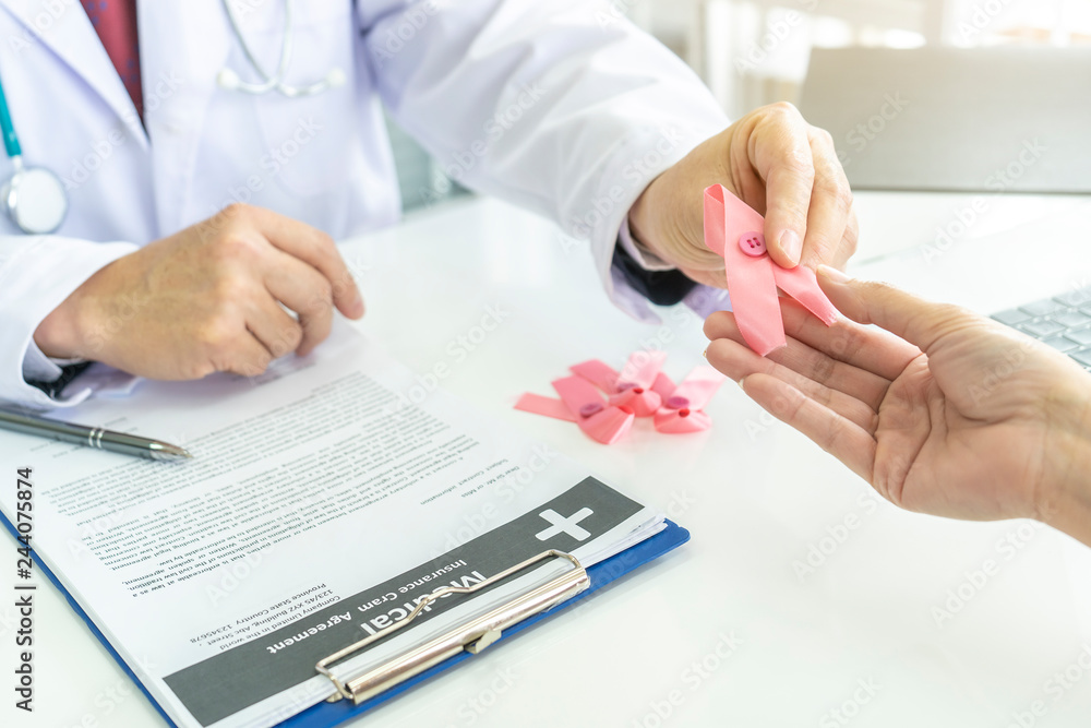 close up hand of Doctor Holds Pink Ribbon given to woman patient while talking raising knowledge with tumor illness. Concept of Pink ribbon for breast cancer awareness or October Pink day,health care close up hand of Doctor Holds Pink Ribbon given to woman patient while talking raising knowledge with tumor illness. Concept of Pink ribbon for breast cancer awareness or October Pink day,health care