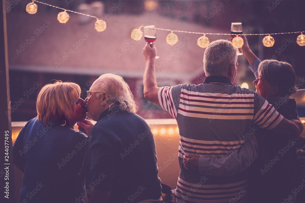 Romantic and love concept with two senior adults couple celebrate together at home in a terrace with city view - toasting with wine and kissing - matures people have fun in friendship outdoor