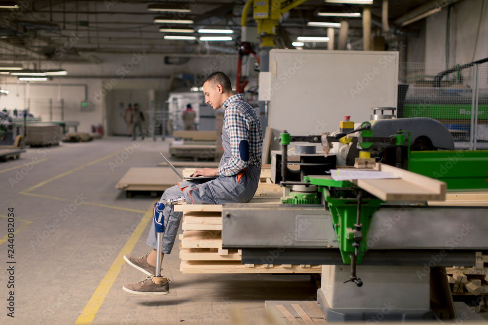 Disabled young man with an artificial leg is working at the furniture factory Disabled young man with an artificial leg is working at the furniture factory