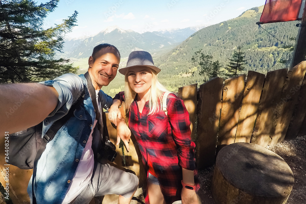 tourism, travel, people, leisure and technology concept - happy international teenage couple taking selfie over alps mountains in austria background