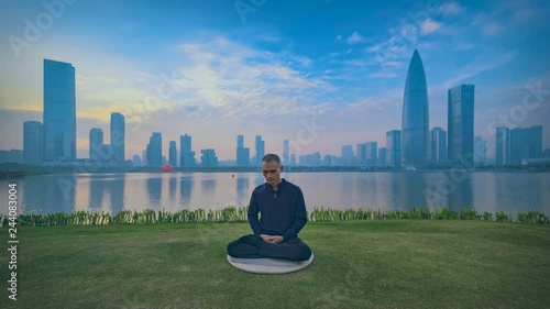 man sitting in Zen on lawn at seaside, close eyes in peace,clouds drifting across the sky,cityscpae with buildings,Shenzhen China photo