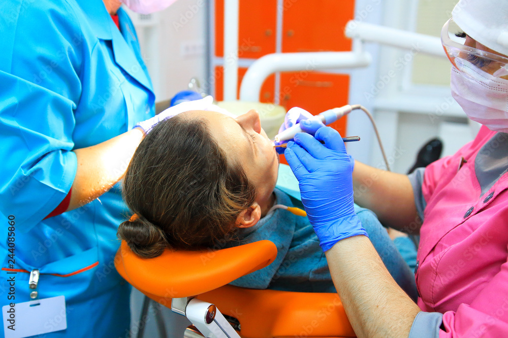 Dentist and his assistant drills teeth of patient Dentist and his assistant drills teeth of patient