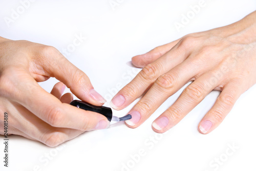 The female hand applies a practically transparent varnish on the nail with a brush. Hands isolated on white background