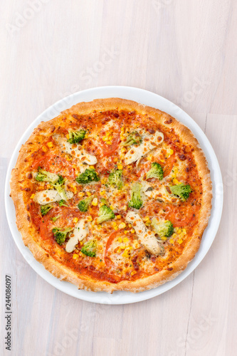 Children's pizza with chicken, corn and broccoli on a light wooden background