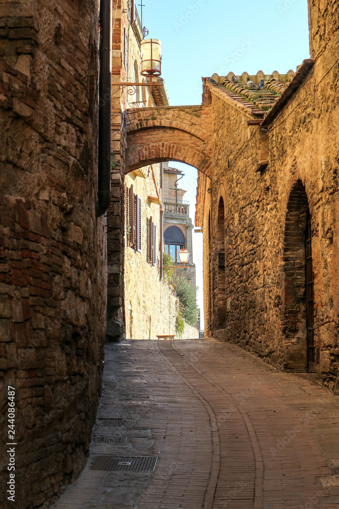 Medieval narrow street with stone walls and arch at sunny winter day, San Gimignano, Tuscany, Italy