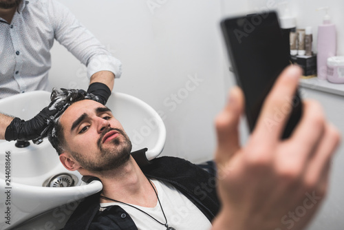 Man using smart phone while having his hair washed in hairdressing salon