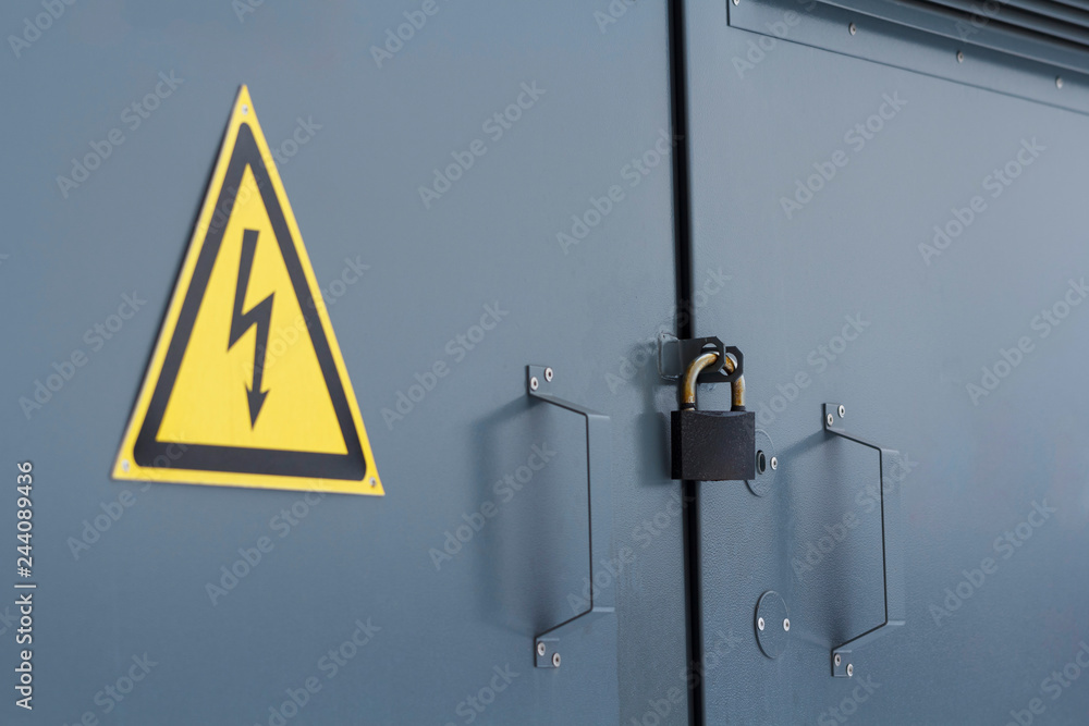Locked electric panel with hazard sign on the grey door of transformer