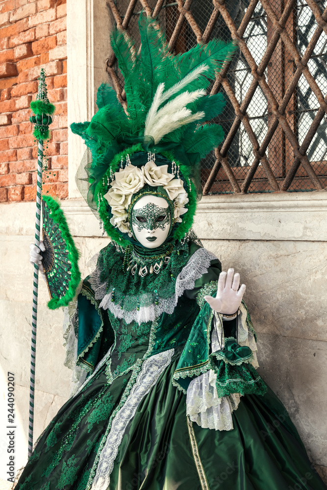 Woman in green dress and mask posing against the wall at Venetian carnival