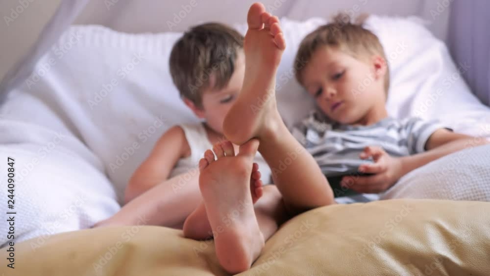 Two boys holding smartphone, tablet sitting on chair, focus on childrens feet. Two boys holding smartphone, tablet sitting on chair, focus on childrens feet.
