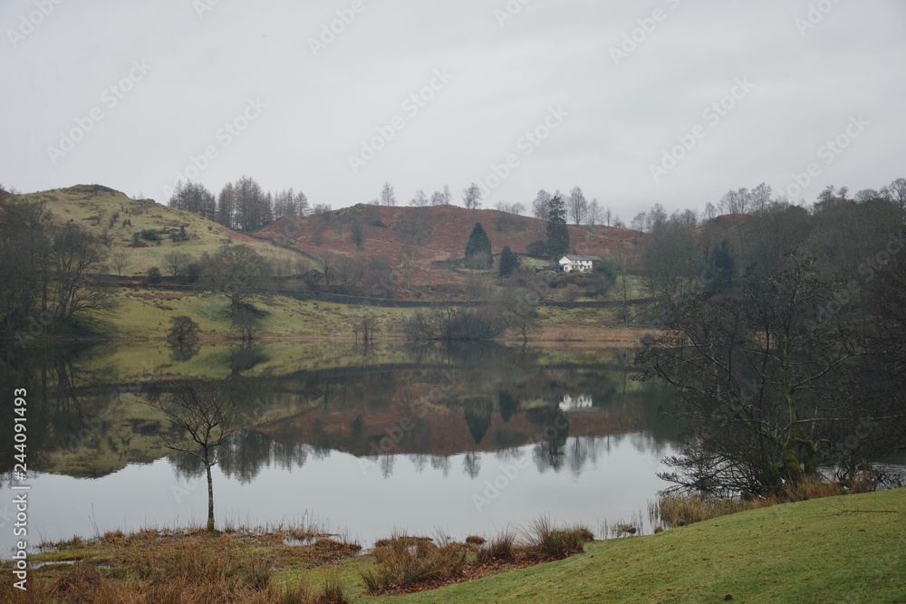 Loughrigg Tarn: small mountain lake and farm house with perfect reflections in Lake District (Cumbria)