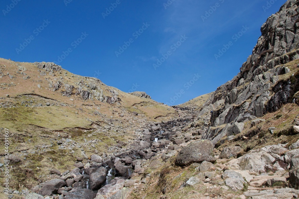 Fast mountain stream tumbling between cliffs in a valley (Lake District, UK) Fast mountain stream tumbling between cliffs in a valley (Lake District, UK)