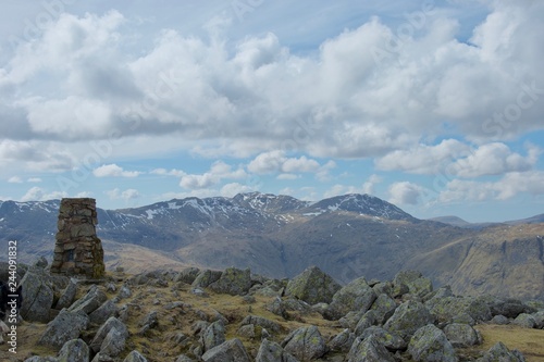 Cairn and rocks at summit of Lake District mountain; snow covered crags in distance