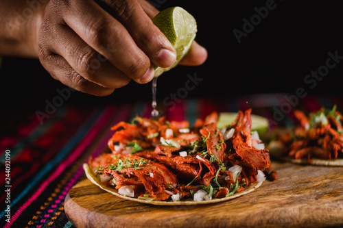 Close-up of a lime being squeezed in a mexican taco, with traditional colorful background