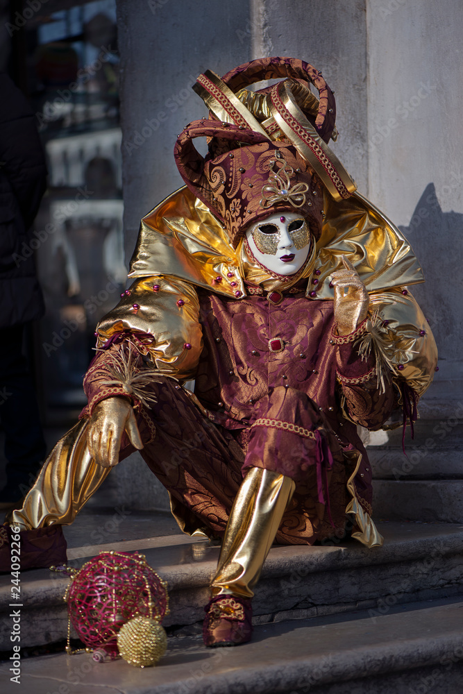 Fototapeta premium Person in carnival costume of Harlequin sits on the steps in the street in Venice, Italy