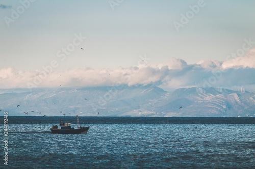 Fishing boat in the sea, under beautiful clouds, Spain's coast in the background (Strait of Gibraltar)