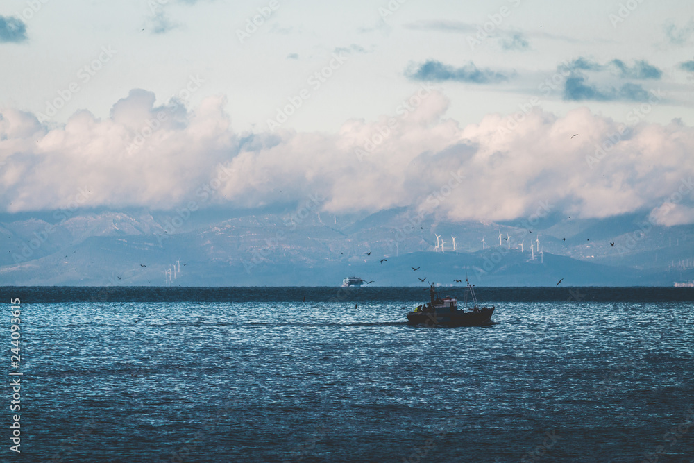 Fishing boat in the sea, under beautiful clouds, Spain's coast in the background (Strait of Gibraltar)