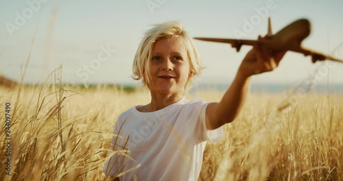 Happy young boy flying his wooden toy airplane in golden field at sunset