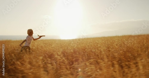 Adorable young boy running through golden field holding wooden airplane