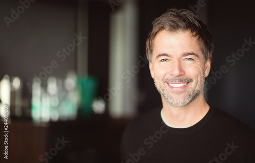 Slika na platnu A portrait of a middle-aged bearded man smiling at the camera on a blur backgrou