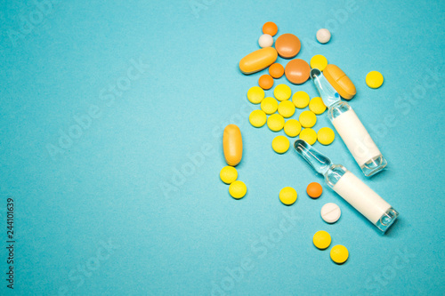 Pills of different colors and ampoules on blue background