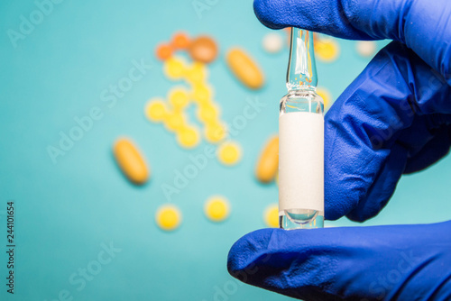 Hand in blue medical glove. The doctor holds one ampoule. blue background with pills