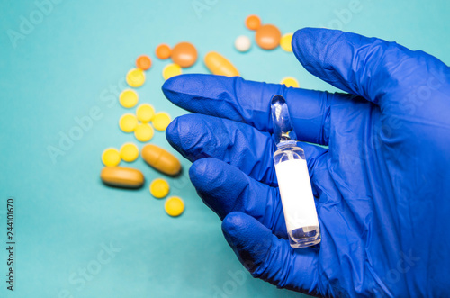 Hand in blue medical glove. The doctor holds one ampoule. blue background with pills