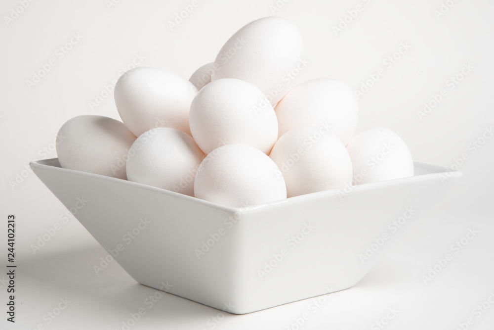 White raw eggs stacked in a rectangular white container set on a white  background.