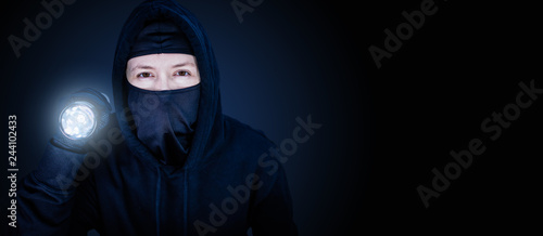 Panorama Einbrecher mit Sturmmaske und Taschenlampe auf blau schwarzen Hintergrund photo