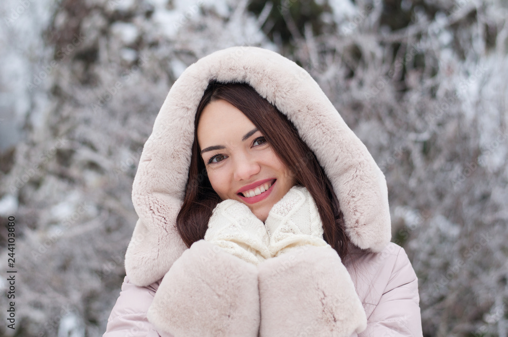 Portrait of young beautiful emotional woman in hooded down coat and gloves on snow covered garden background. Winter snowy landscape Portrait of young beautiful emotional woman in hooded down coat and gloves on snow covered garden background. Winter snowy landscape