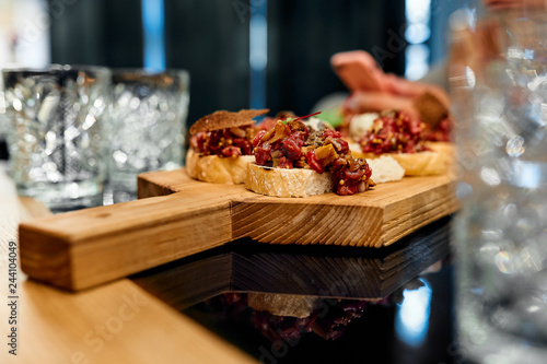 Appetizer in the form of meat bruschetta on a wooden board and empty glass goblets 