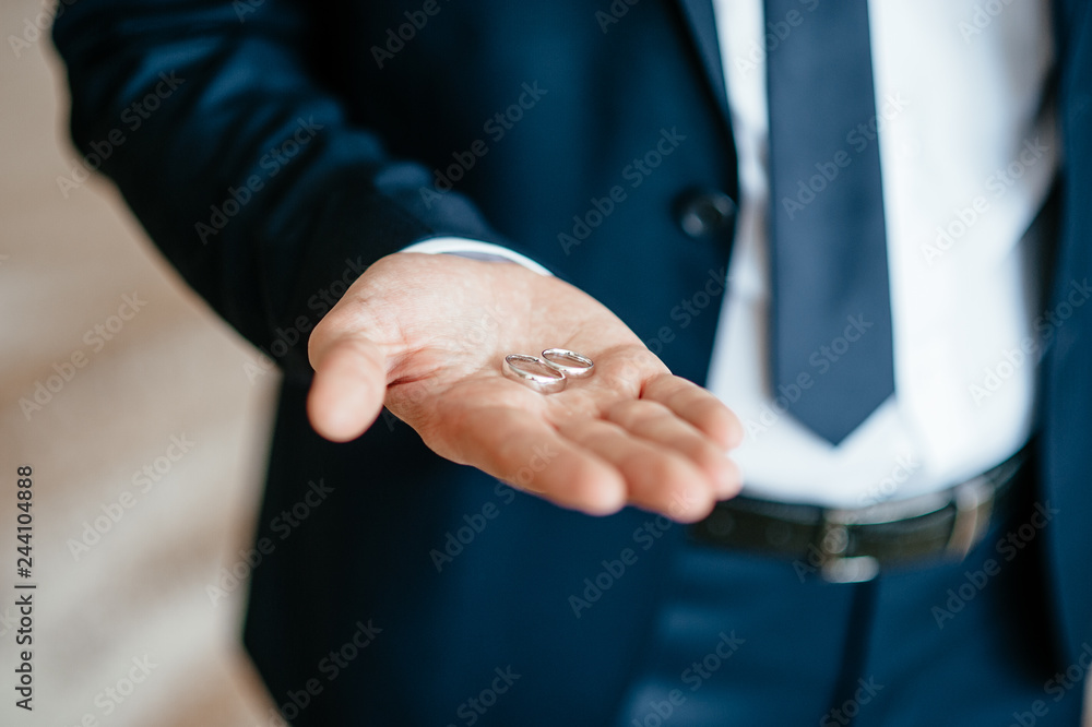 groom's hand holds wedding rings. soft focus
