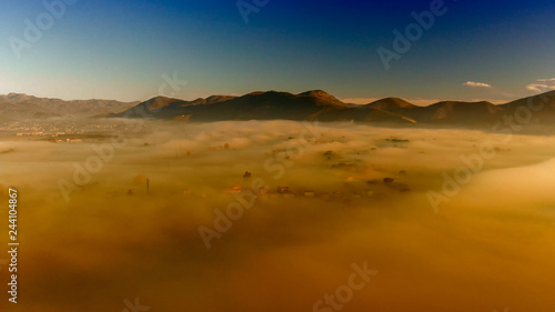 Panoramic aerial view of countryside scenario surrounded by fog, view from drone above the clouds