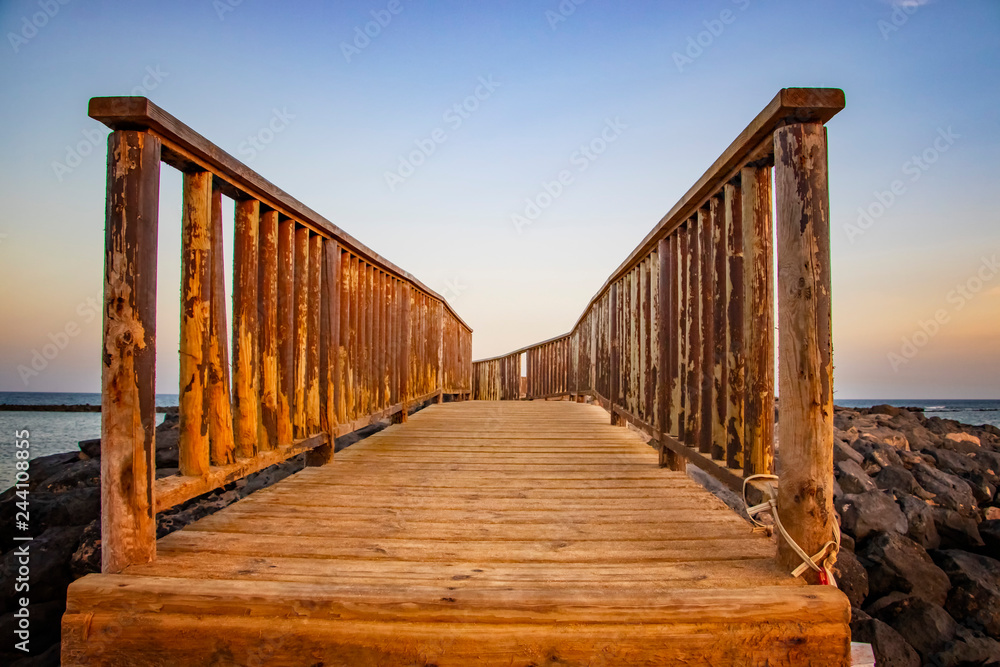 Obraz premium The wooden bridge overlooking the sea leads to an island at sunset.