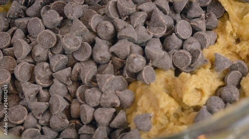 Adding chocolate chip morsels to cookie dough in an electric stand mixer in 4k. The kitchen appliance mixes bittersweet chocolate pieces into raw batter. Top down view for step by step gif recipes.